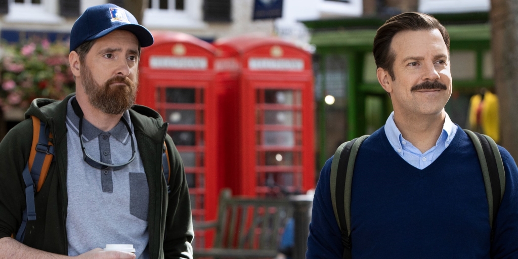 Jason Sudeikis and Brendan Hunt star in Apple TV's Ted Lasso as Ted and Coach Beard, friends and football coaches standing in front of some red telephone boxes 